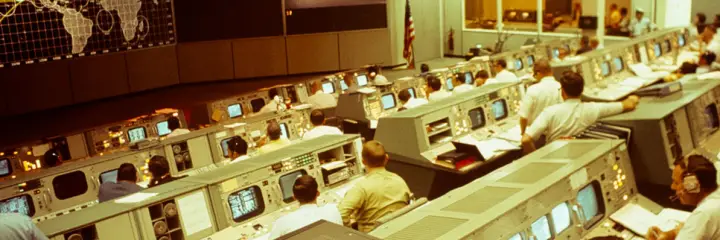 Engineers at their consoles in a 1960s mission control room